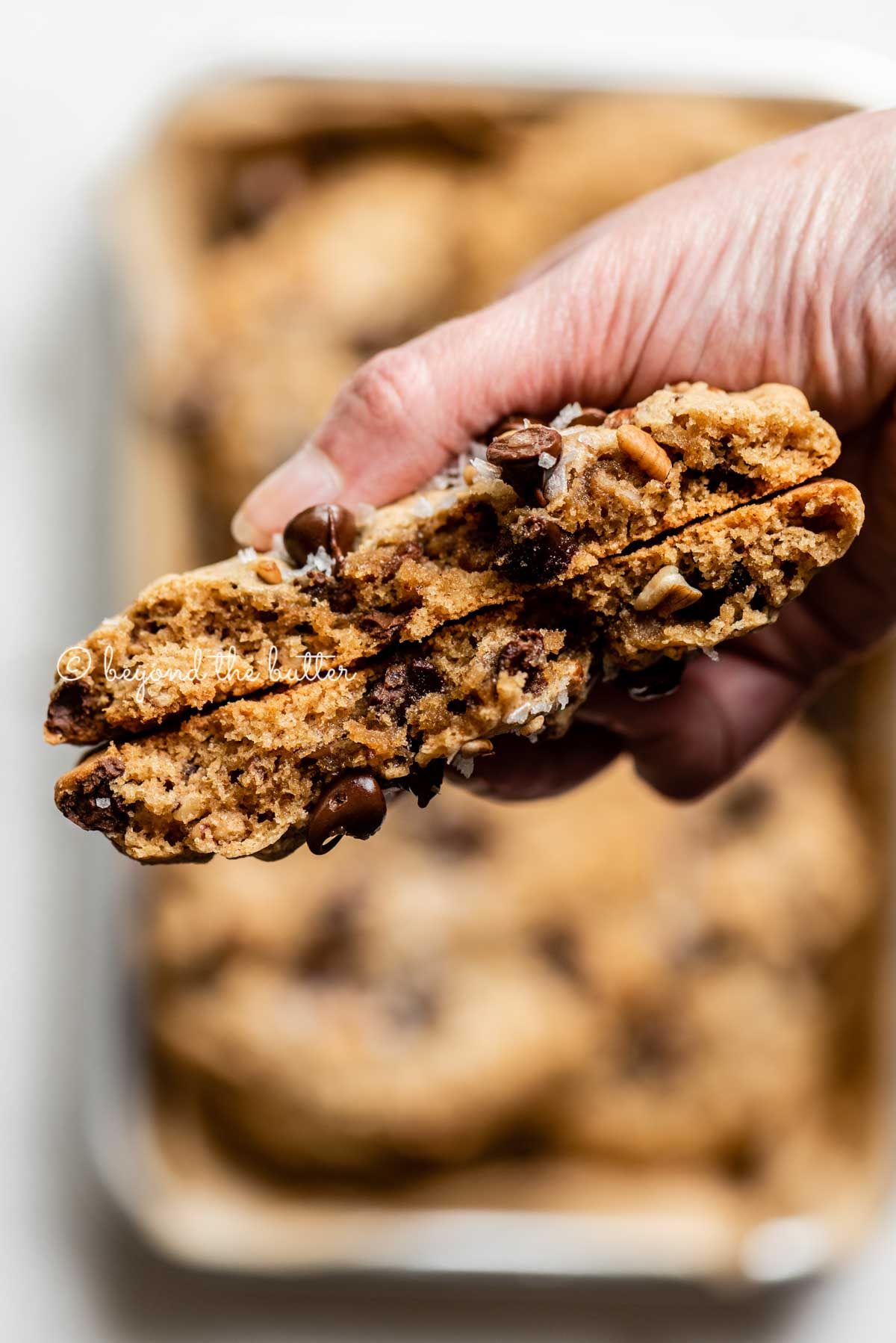 Hand holding a large almond butter chocolate chip pecan cookie that's been split in half | All images © Luyiz™