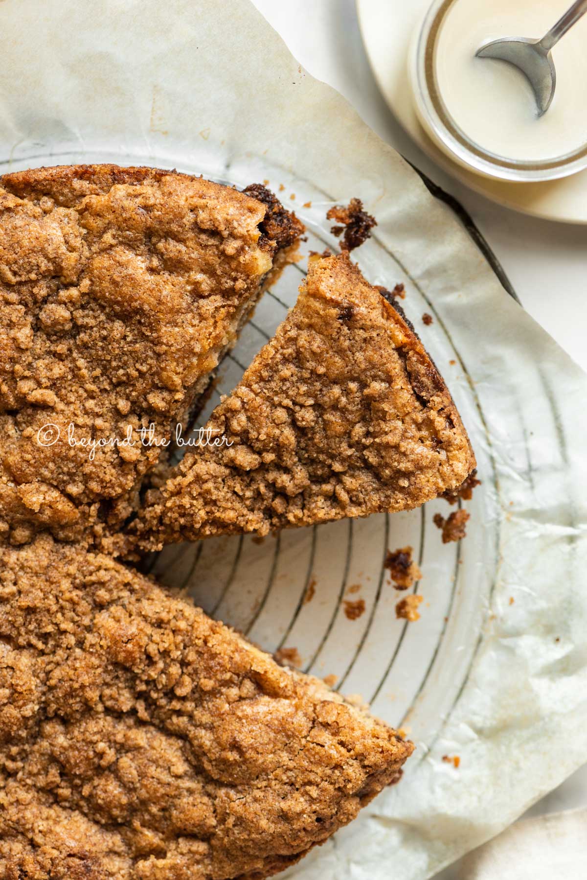 Apple coffee cake on a parchment paper lined wire cooling rack with slices removed and a simple vanilla glaze to the side | All Images © Luyiz™