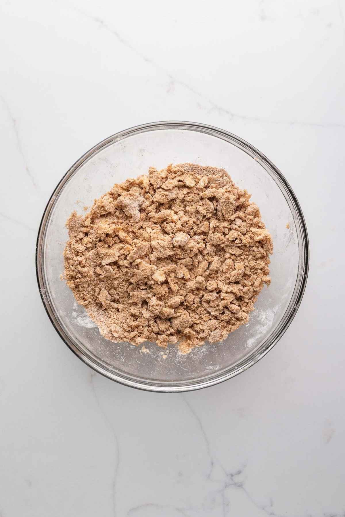 Cinnamon streusel topping in a medium glass mixing bowl on a light grey marbled background.