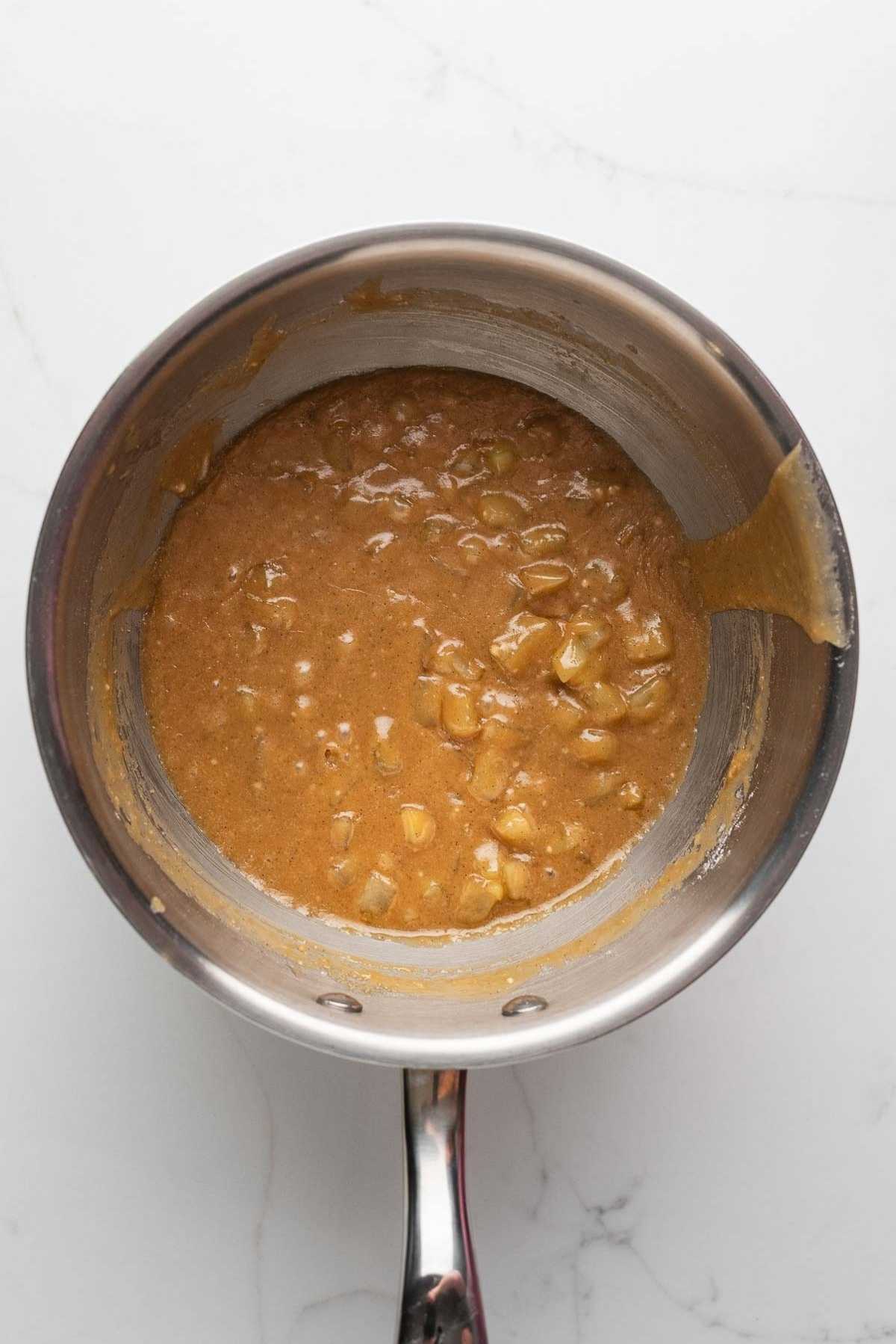 Caramel apple glaze in a medium saucepan on a light grey marbled background.
