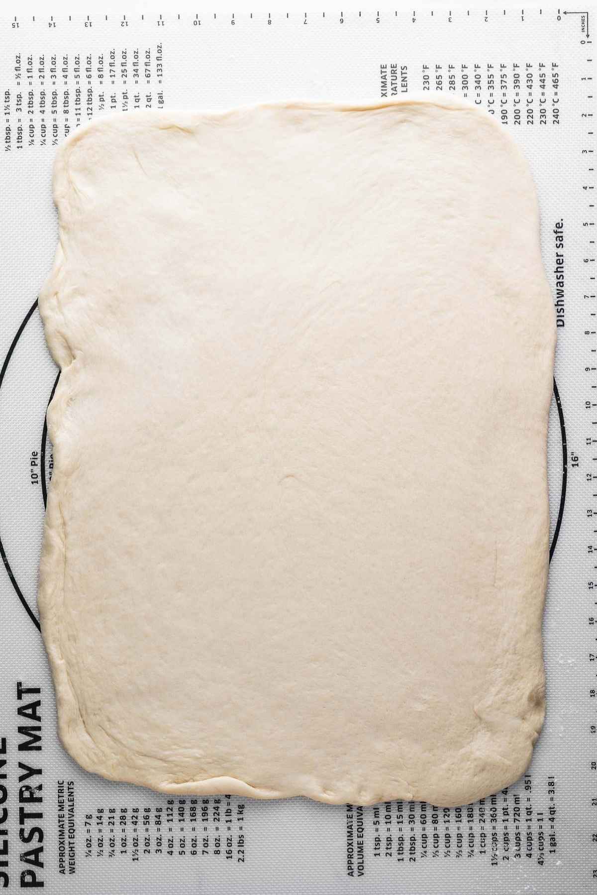 Cinnamon roll dough rolled out to an eighteen inch by 12 inch rectangle on a silicone mat.