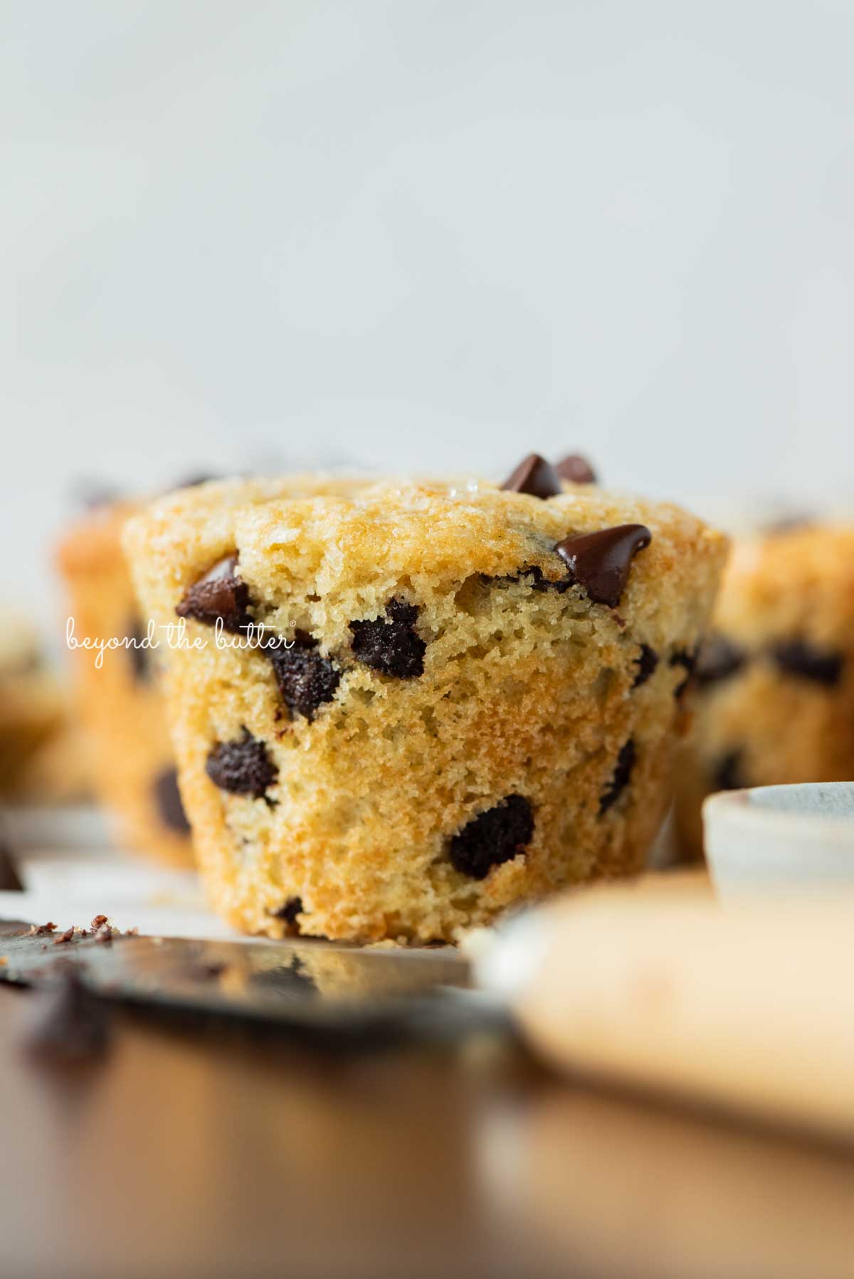 Single unwrapped bakery style chocolate chip muffin on a flattened muffin liner with white background | © Luyiz®