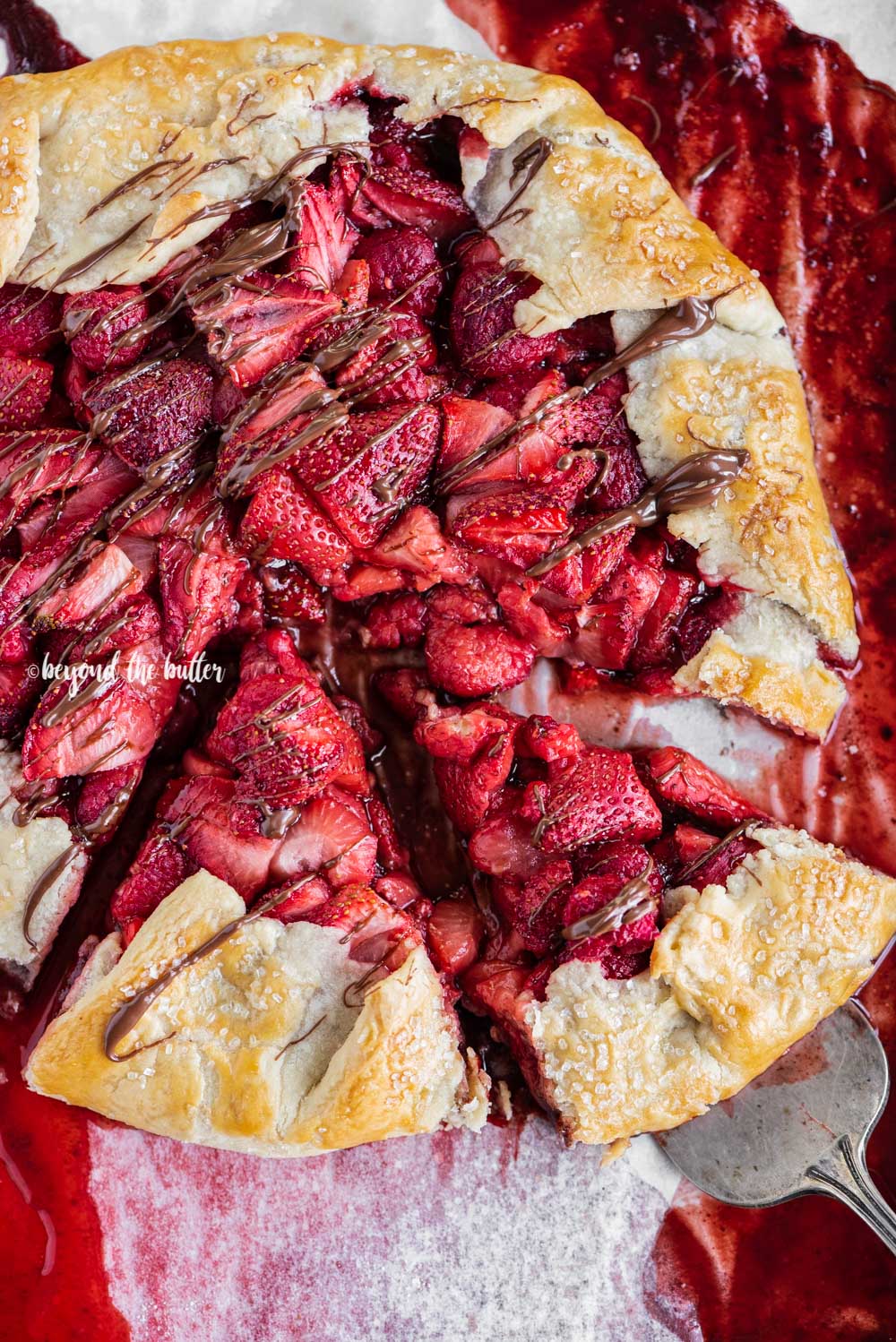 Overhead image of a Berry Nutella Galette on a baking sheet with Nutella drizzled over the top and 2 slices cut | All Images © Luyiz™