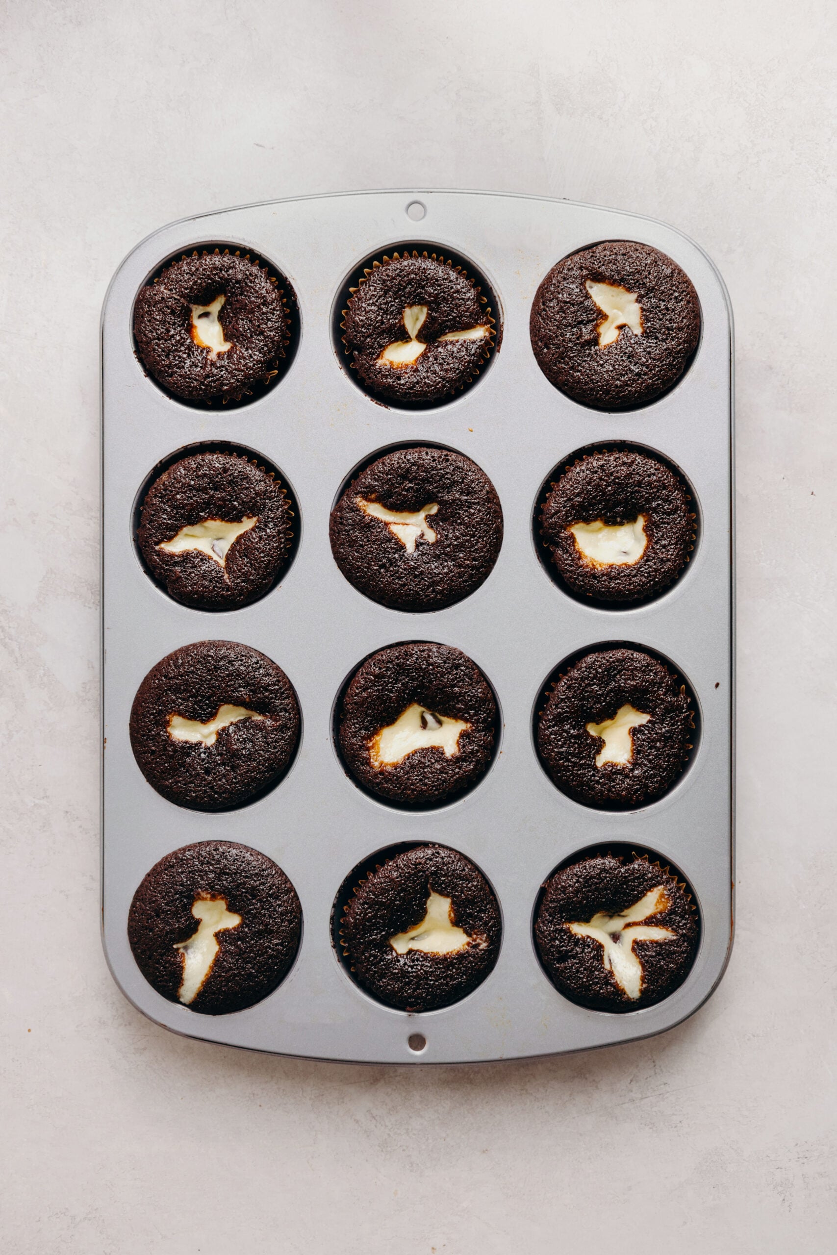 Baked black bottom cupcakes in a metal cupcake tin on a white marbled background.