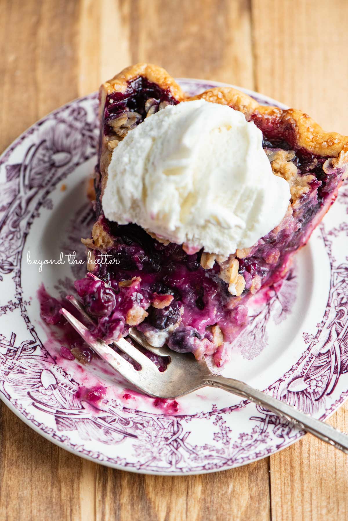 Half eaten slice of blueberry crumble pie with scoop of vanilla bean ice cream on top | © Luyiz®