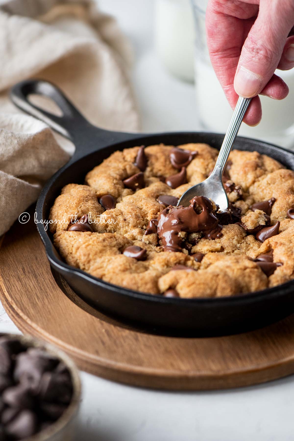 Warm brown butter chocolate chip skillet cookie with two spoons resting in skillet on wood trivet | All Images © Luyiz®