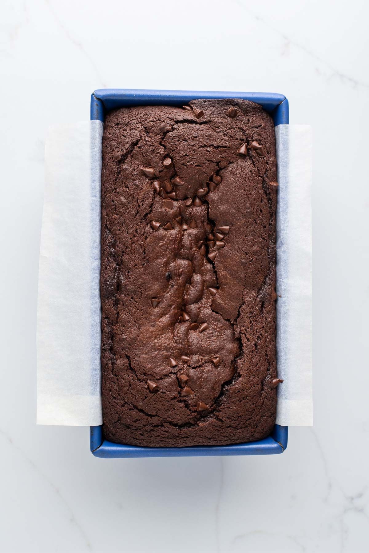 Baked brownie bread in a blue metal loaf tin on a white marbled background.