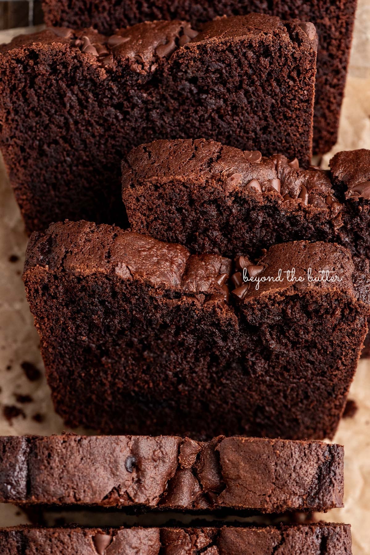 Slices of dense fudgy brownie bread on a brown parchment paper lined cooling rack on a wood background.