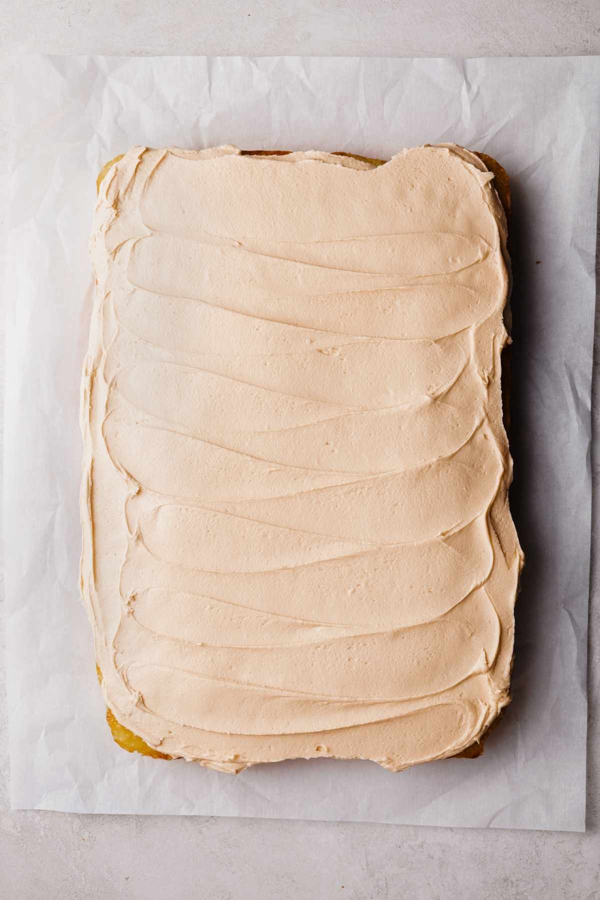 Frosted butterscotch krimpet sheet cake on a parchment paper lined white and grey textured background.