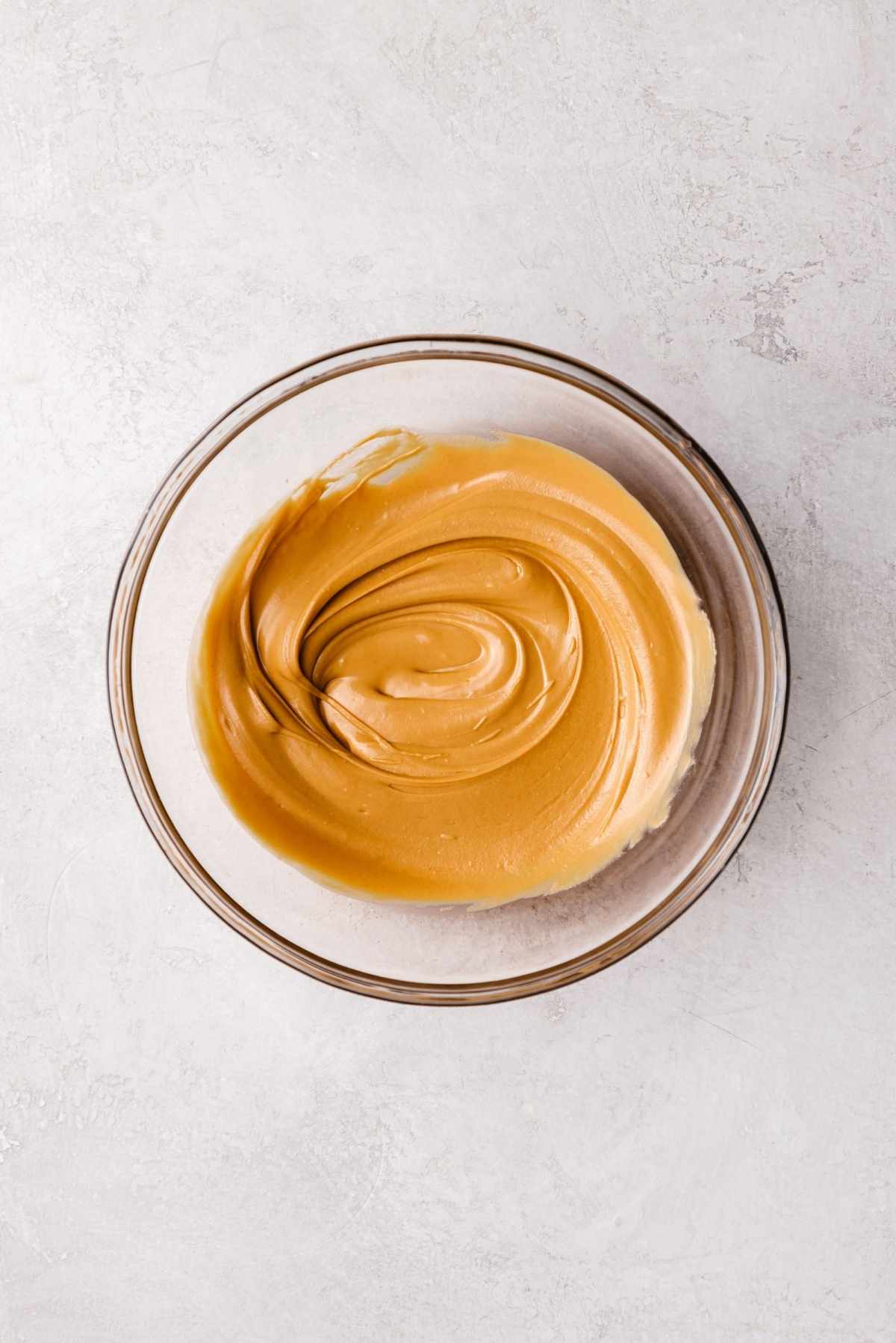 Melted butterscotch chips in a small glass bowl on a white and grey textured background.