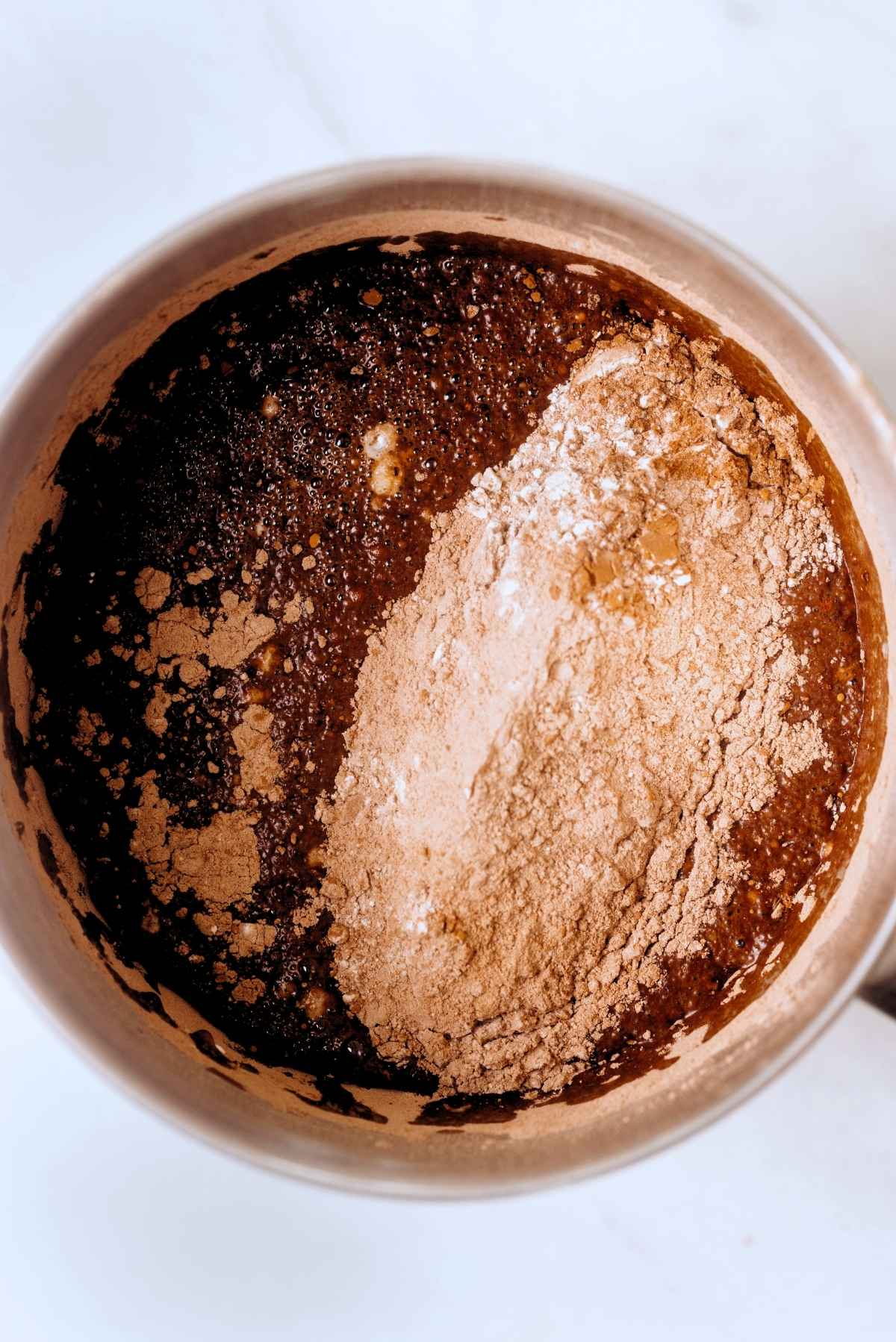 Chocolate cake dry ingredients added to stainless steel mixing bowl with wet ingredients.
