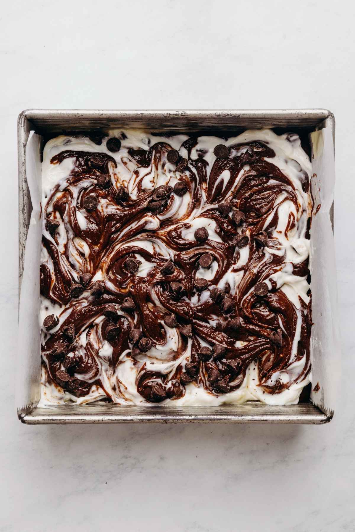 Chocolate chip cream cheese filling swirled into brownie batter in a parchment paper lined baking tin.