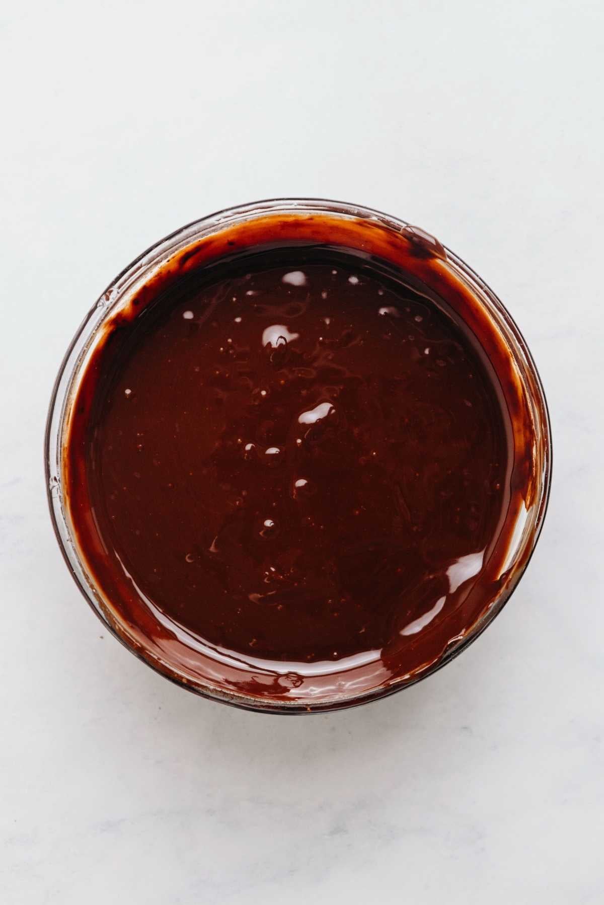Melted butter and chocolate with whisked in cocoa powder in a small glass microwaveable bowl on a white and grey marbled background.