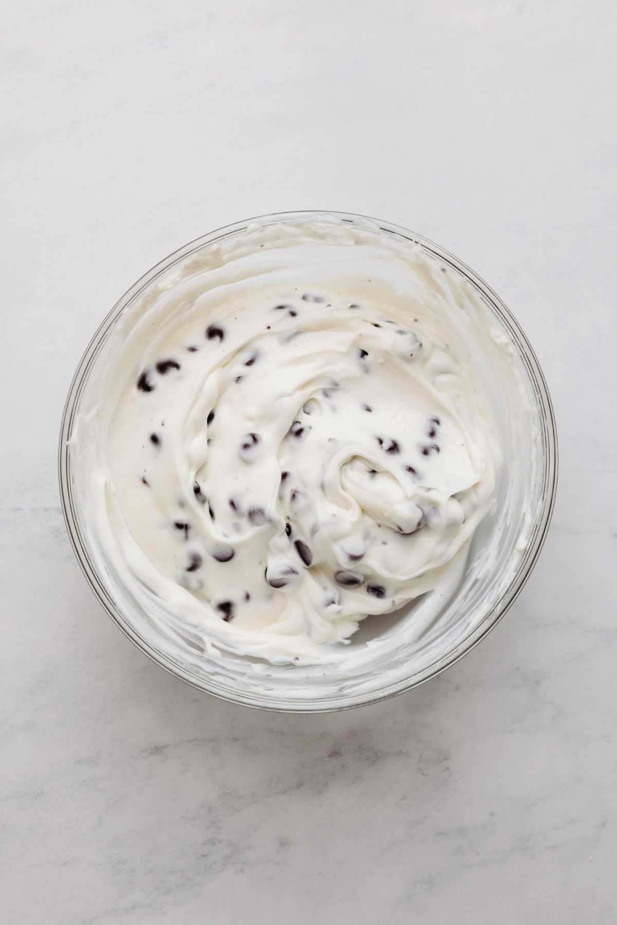 Chocolate chip cream cheese filling in a large glass mixing bowl on a white and grey marbled background.