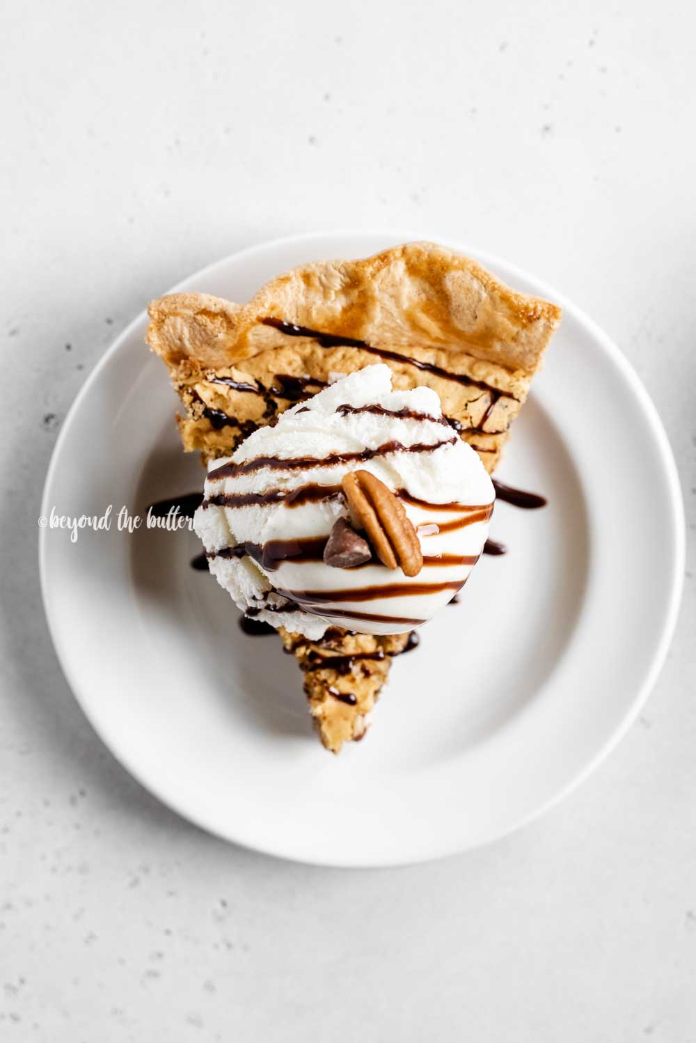 Overhead image of one slice of chocolate chip pie with a scoop of vanilla ice cream on top drizzled with chocolate syrup | All Images © Luyiz™