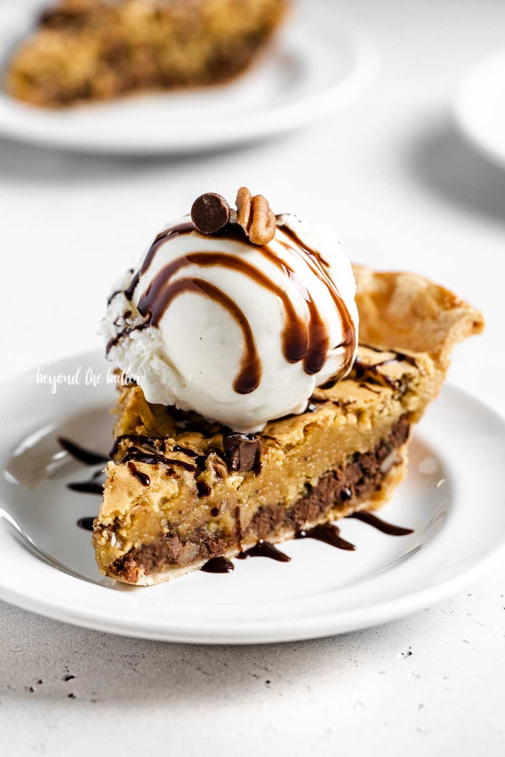 Angled closeup image of Chocolate Chip Pie with a scoop of vanilla ice cream on top that's drizzled with chocolate syrup | All Images © Luyiz™