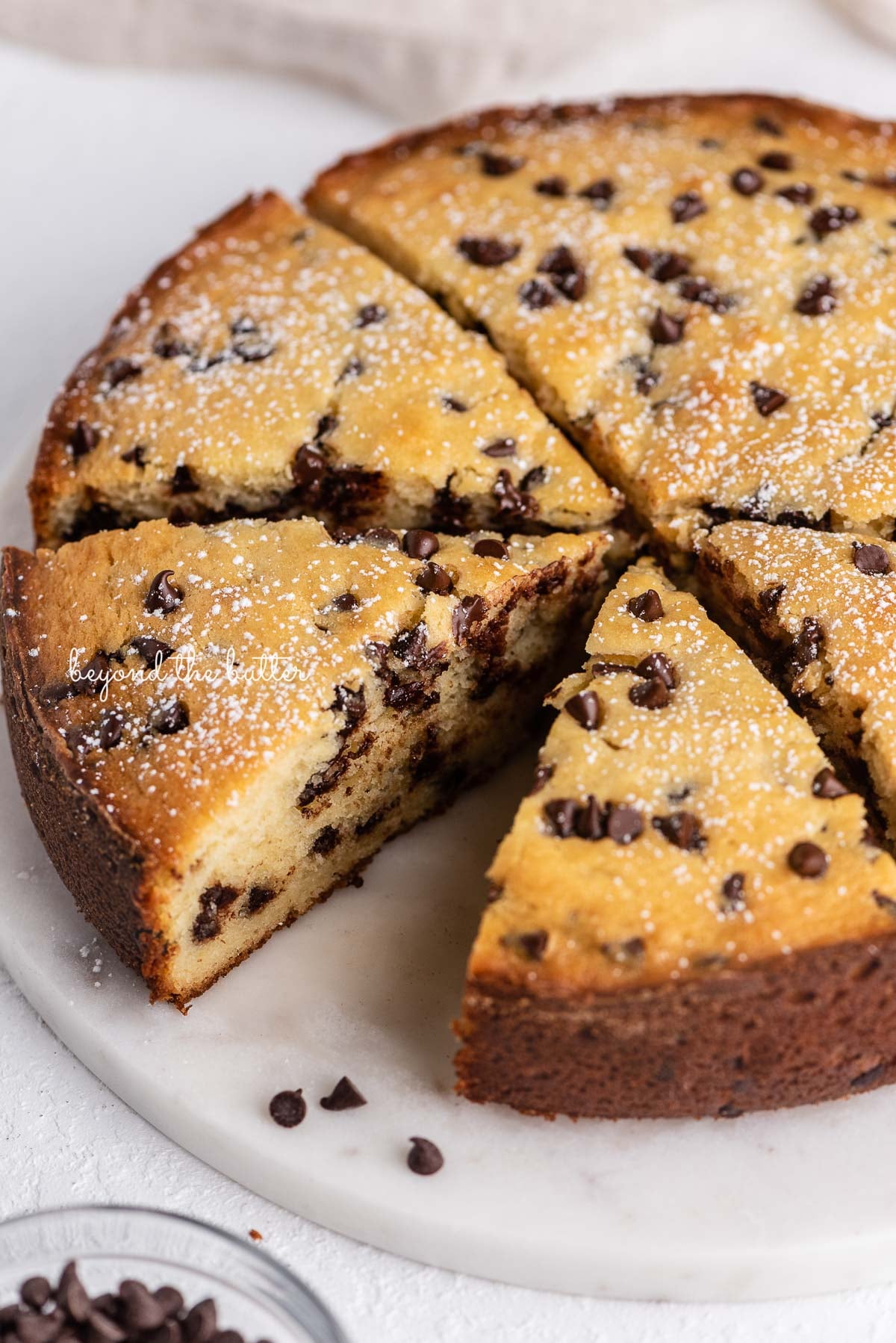 Sliced chocolate chip ricotta cake on a marble cake round with small bowl of mini chocolate chips nearby | © Luyiz®