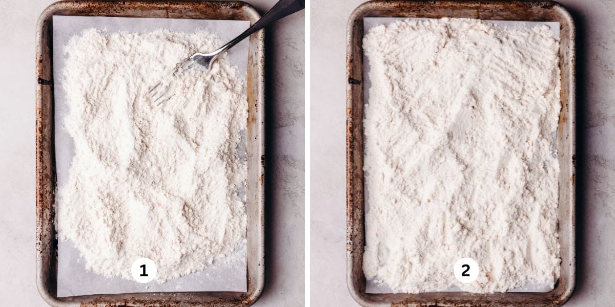Heat treating all purpose flour, stirring with a fork to avoid clumping, on a white parchment paper lined vintage baking sheet on a white marbled background.