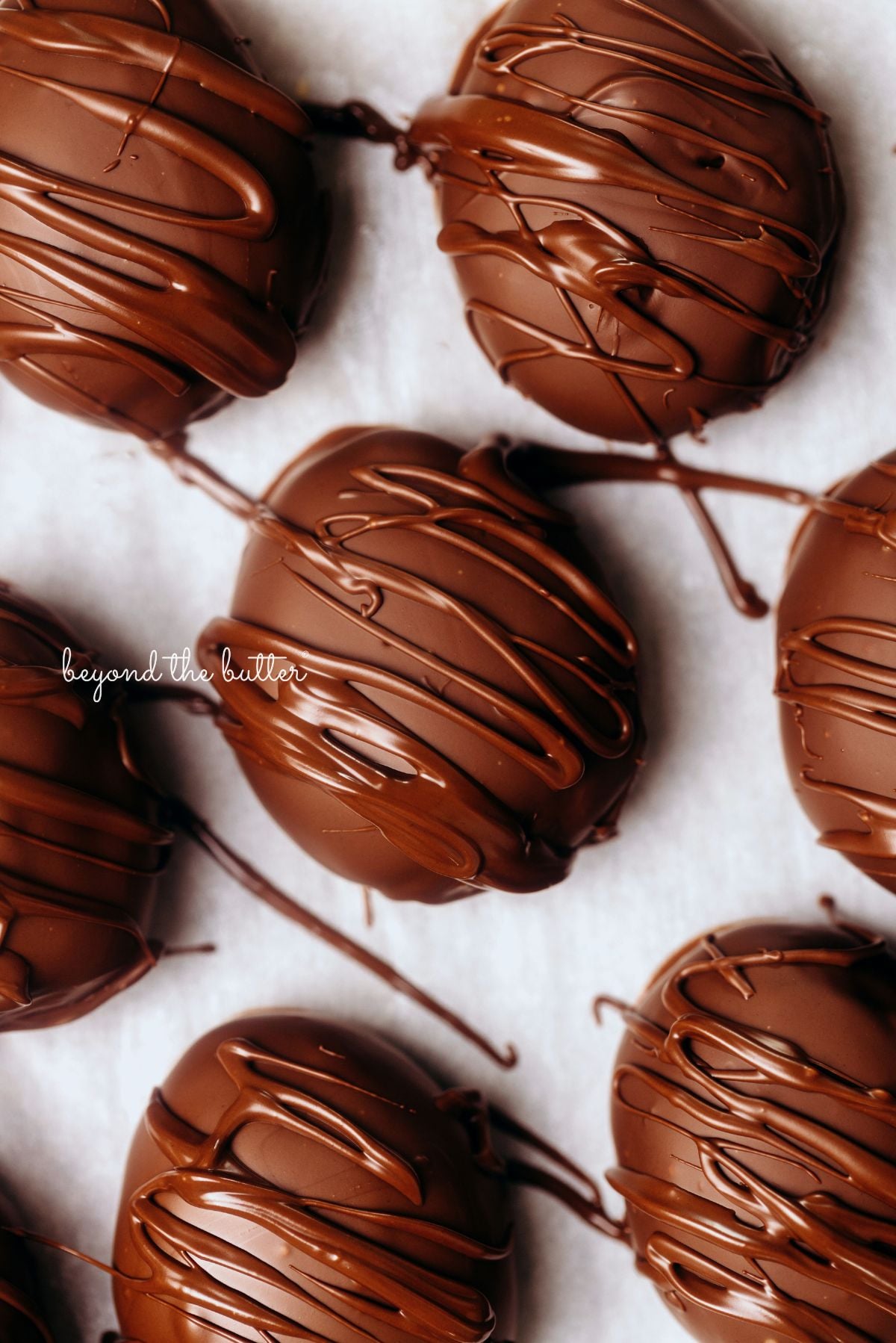 Chocolate covered peanut butter eggs drizzled in extra chocolate and placed on wax paper lined background.