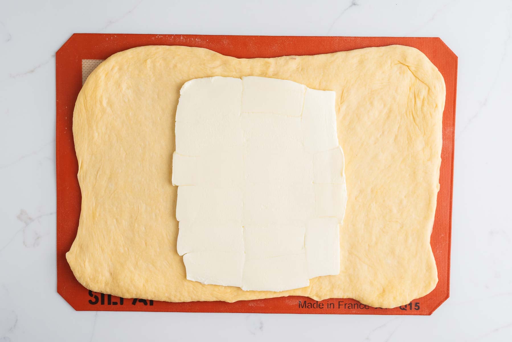 Rolled out croissant dough into a ten inch by 14 inch rectangle with a rectangular slab of butter placed in the center third section of the dough on a silicone baking sheet.