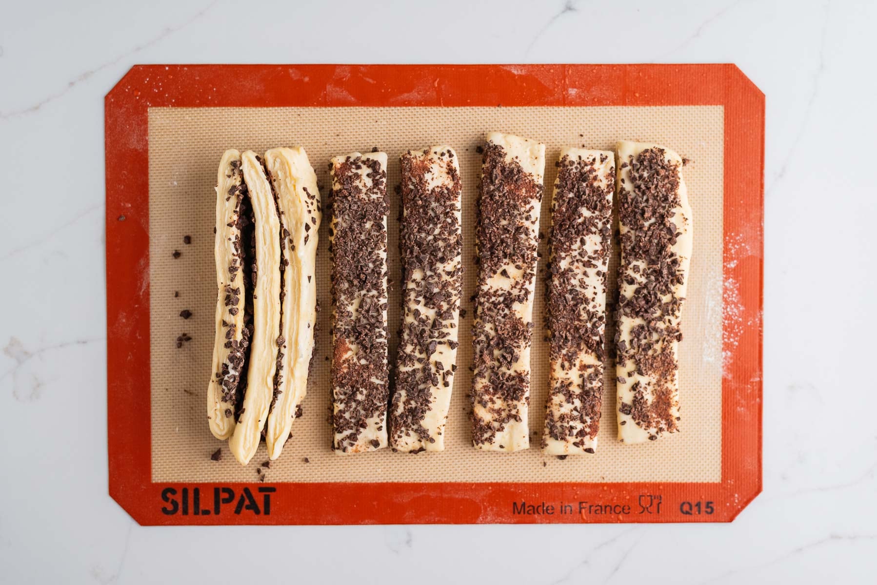 Laminated croissant loaf dough cut into strips and coated with finely chopped dark chocolate then placed on their sides.