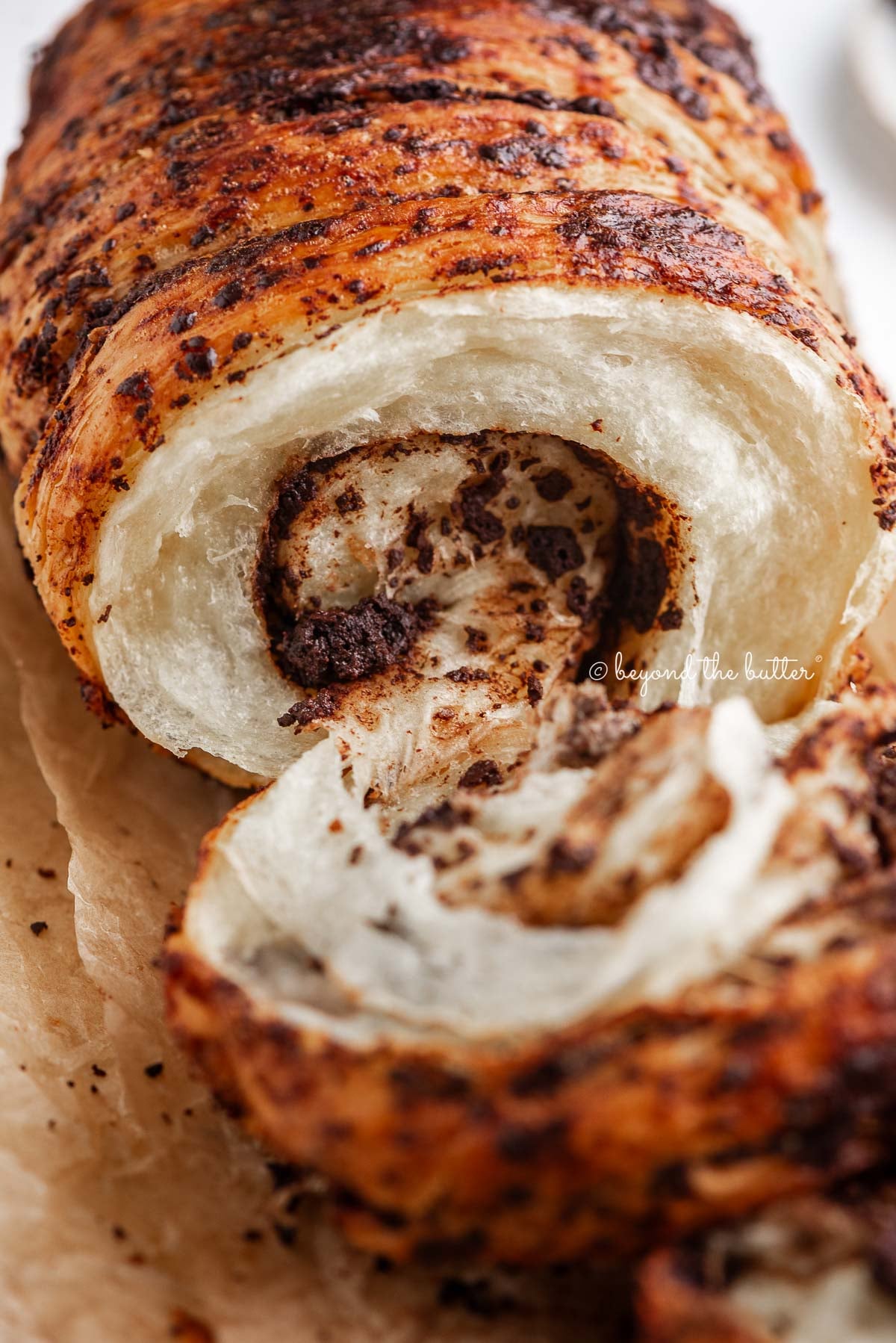 Chocolate croissant loaf pulled apart to see the inside chocolatey, flaky layers on brown parchment paper.