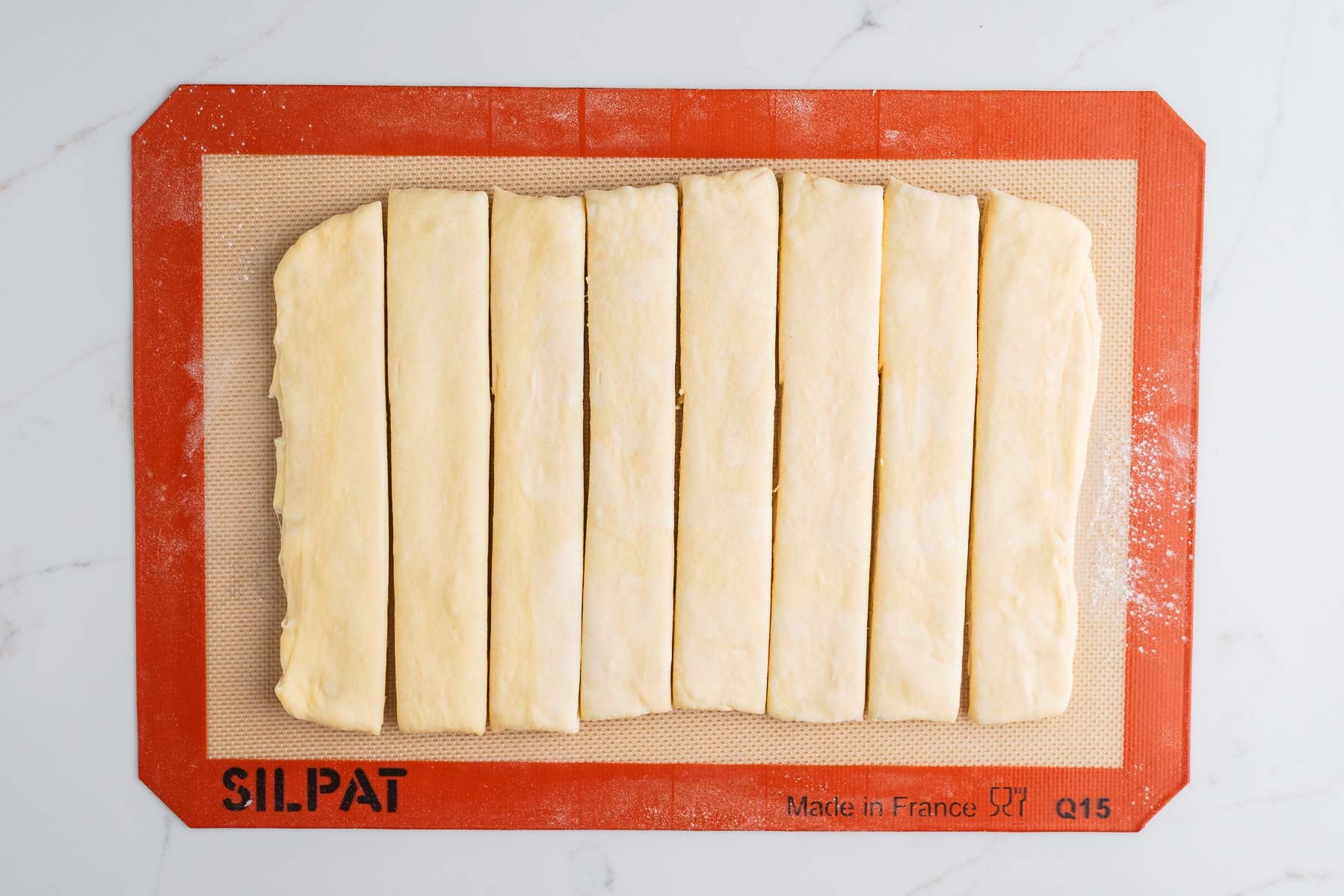 Rolled out laminated croissant loaf dough and cut into eight equally sized strips on a silicone baking sheet.