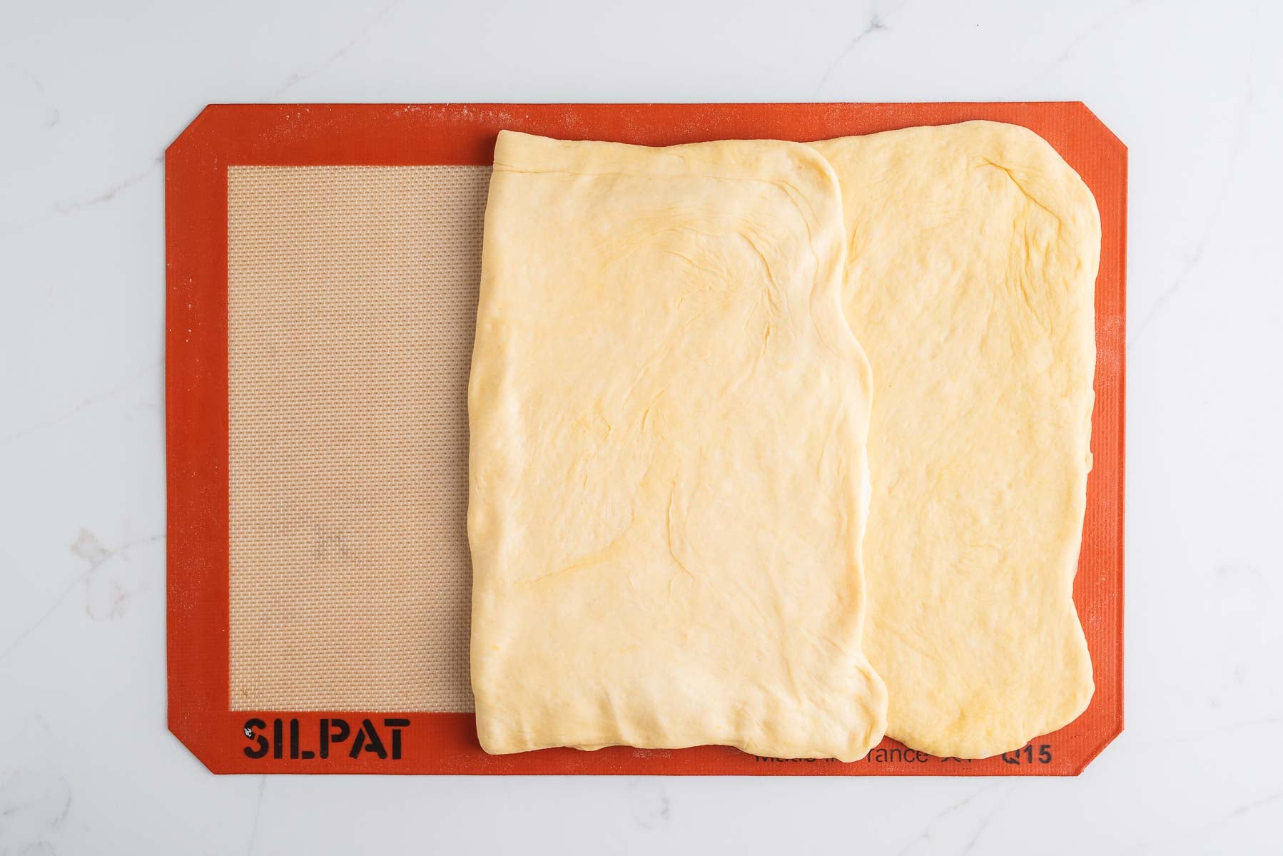 Left panel of dough folded over the rectangular slab of butter on a silicone baking sheet.