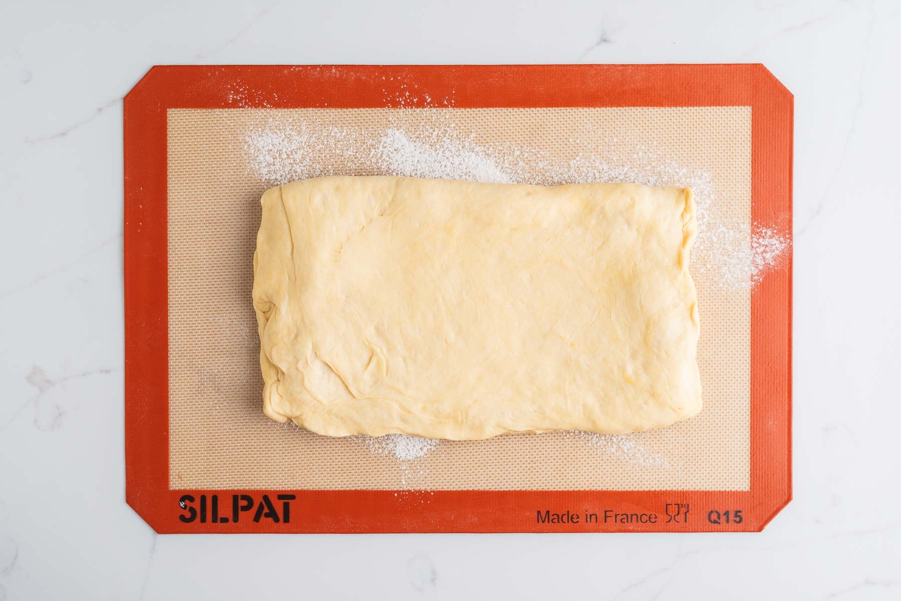 Laminated croissant dough rotated lengthwise to roll out to a nine inch by twelve inch rectangle on a bread flour sprinkled silicone baking sheet.