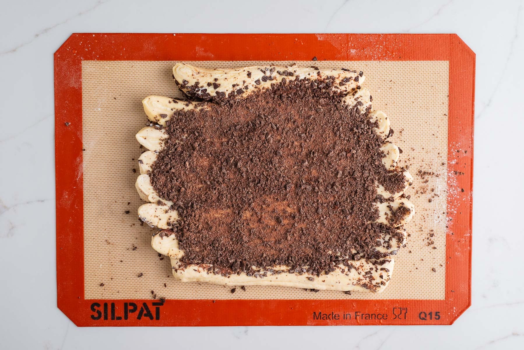 Rotated strips of laminated dough coated with finely chopped dark chocolate pressed together lengthwise, rolled out, then coated again with leftover chopped chocolate.