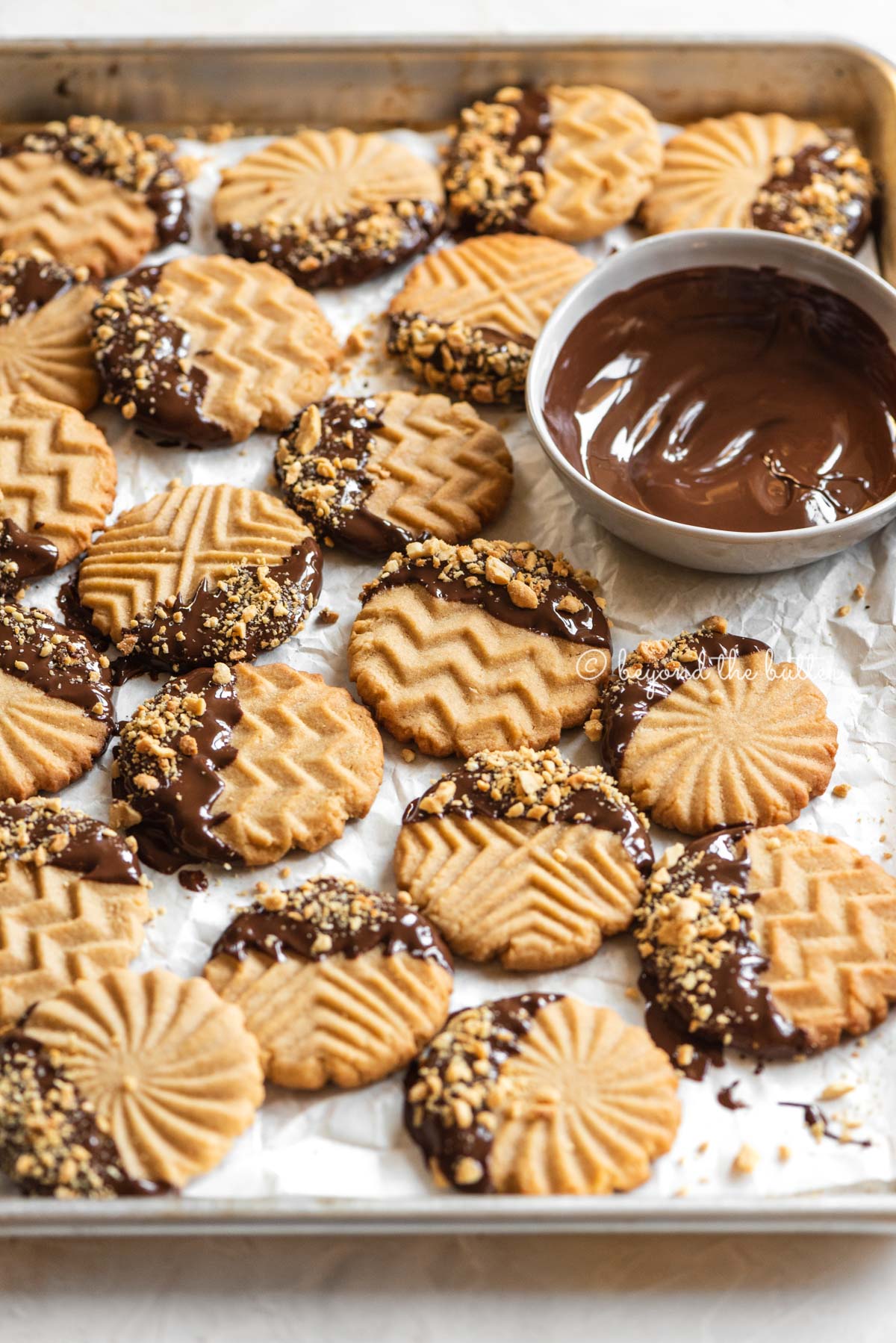Baking sheet with randomly placed chocolate dipped peanut butter cookies with bowl of chocolate nearby | All Images © Luyiz®