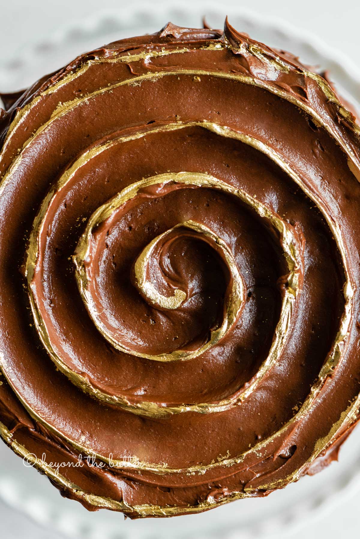 Overhead closeup image of chocolate zucchini cake with chocolate chips and gold decorative swirl on top | All Images © Luyiz™