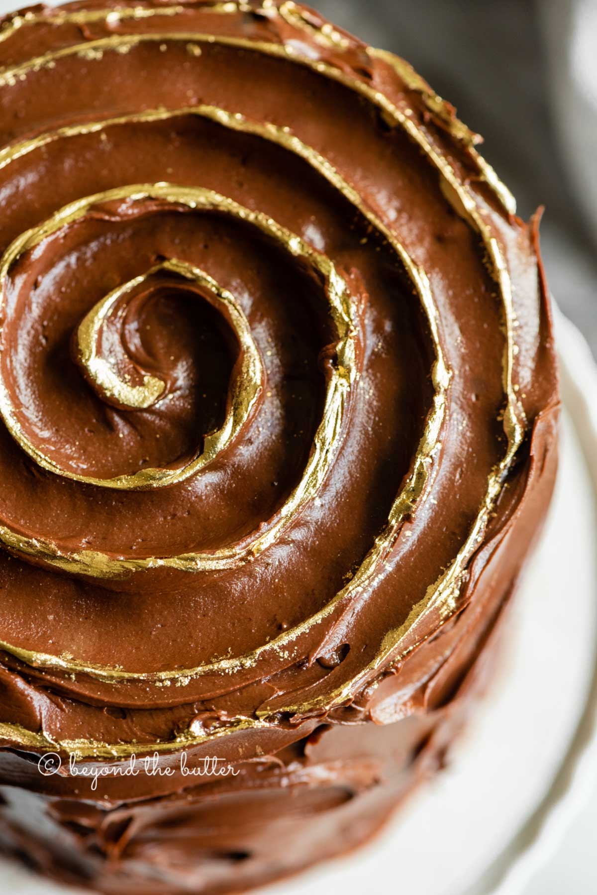 Angled closeup image of chocolate zucchini cake with gold decorative swirl on top | All Images © Luyiz™
