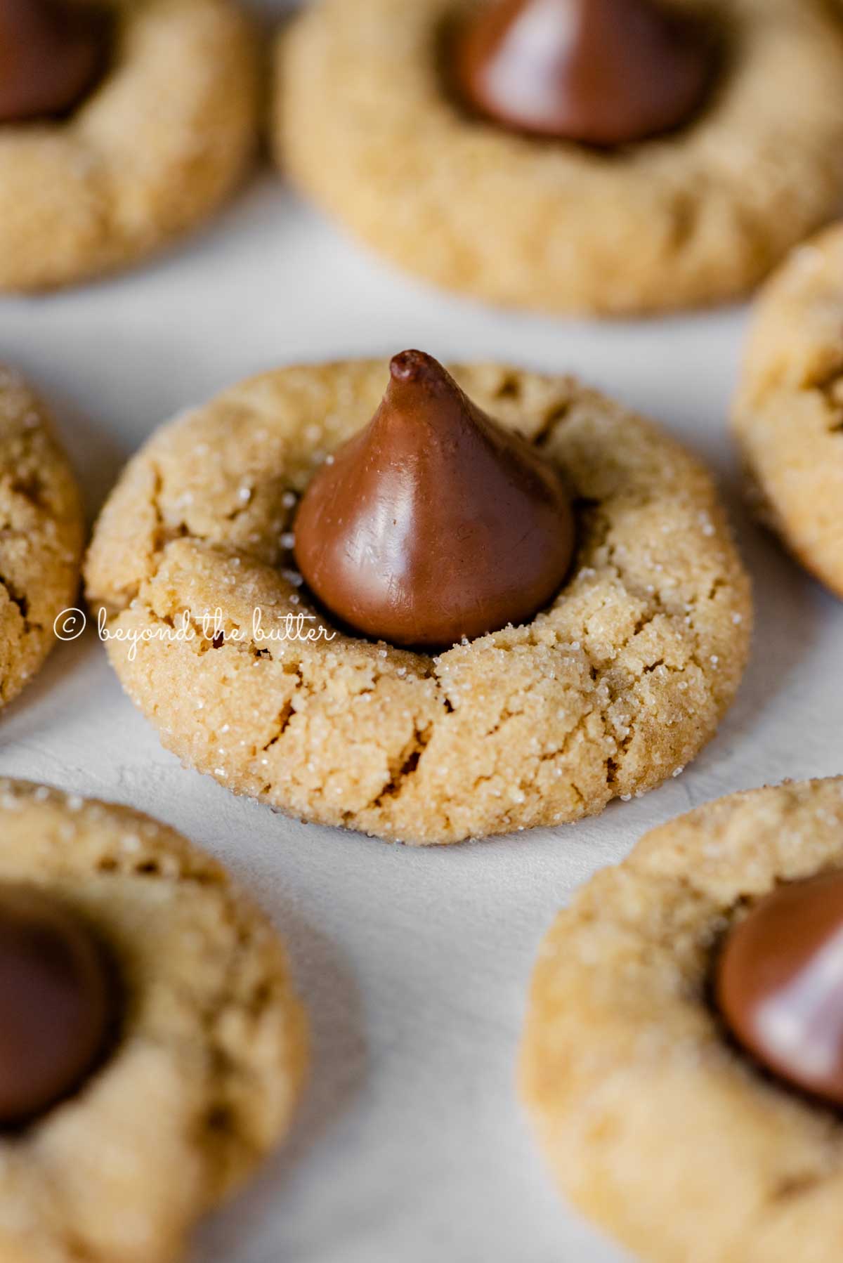 Angled closeup image of peanut butter blossoms on parchment paper lined baking sheet | All Images © Luyiz™