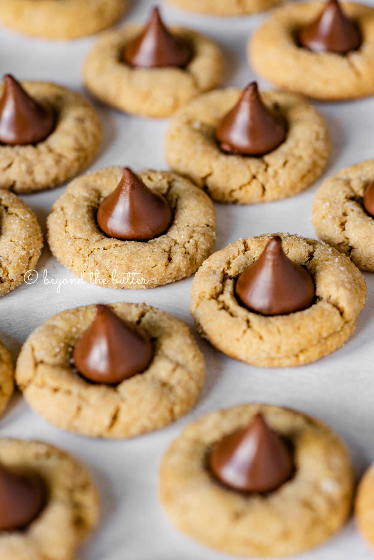 Angled image of peanut butter blossoms on parchment paper lined baking sheet | All Images © Luyiz™