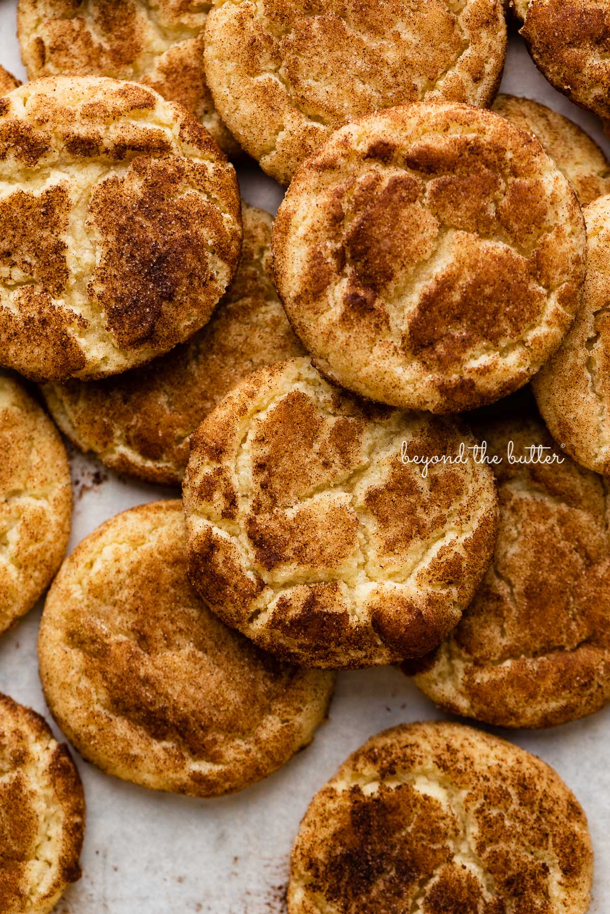 Piled snickerdoodle cookies on a parchment paper lined baking sheet | © Luyiz®