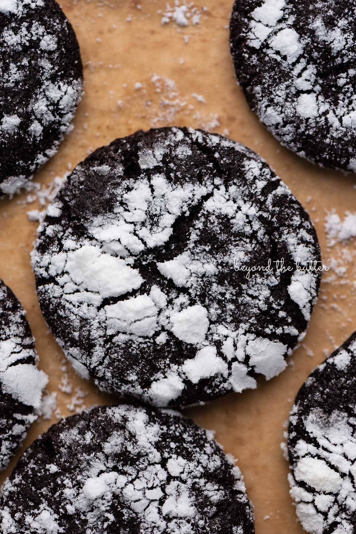 Closeup of dark chocolate crinkle cookie on a brown parchment paper lined baking sheet | © Luyiz®