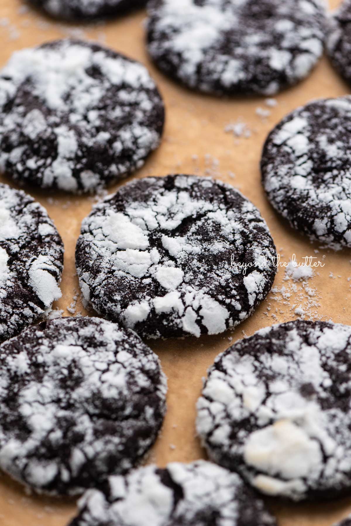 Dark chocolate crinkle cookies on a brown parchment paper lined baking sheet | © Luyiz®