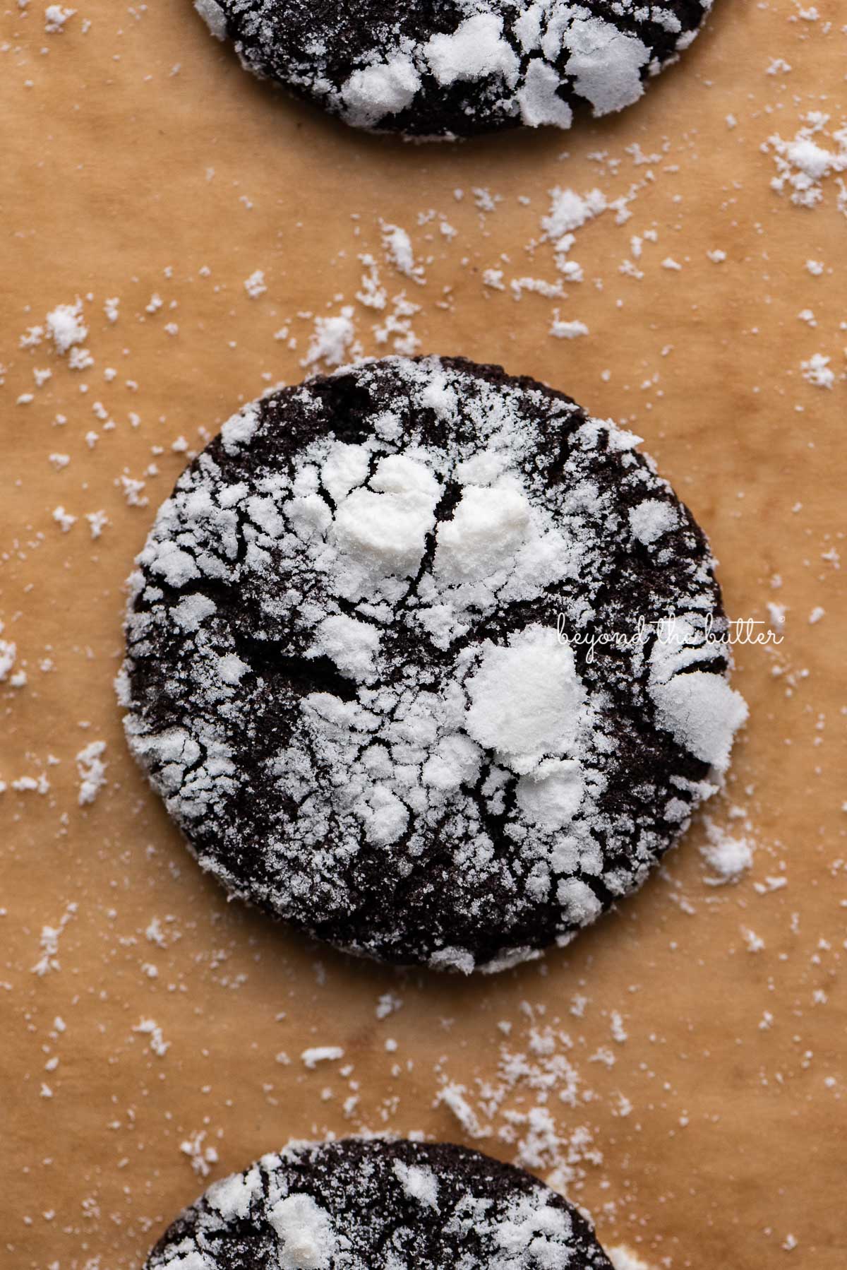 Closeup of dark chocolate crinkle cookie on a brown parchment paper lined baking sheet | © Luyiz®