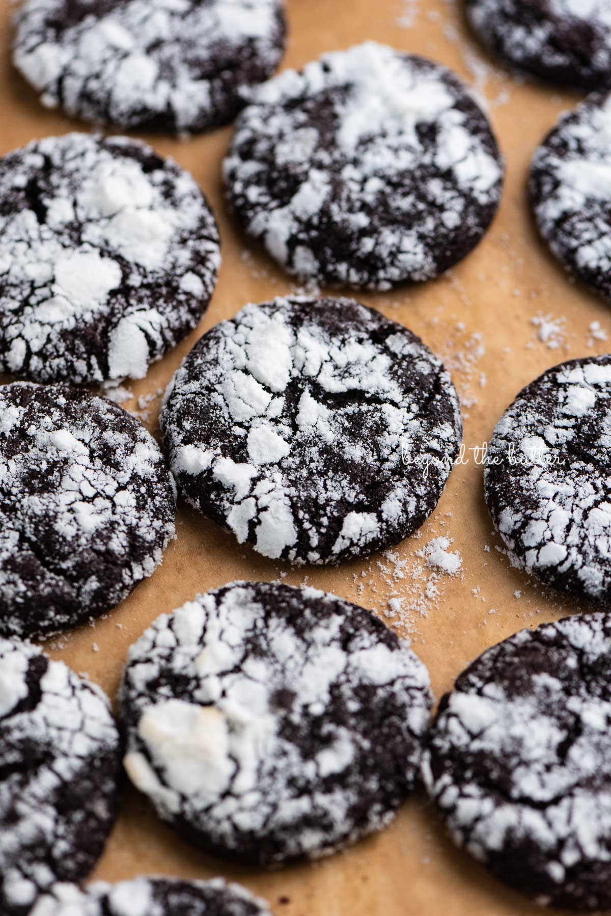 Dark chocolate crinkle cookies on a brown parchment paper lined baking sheet | © Luyiz®