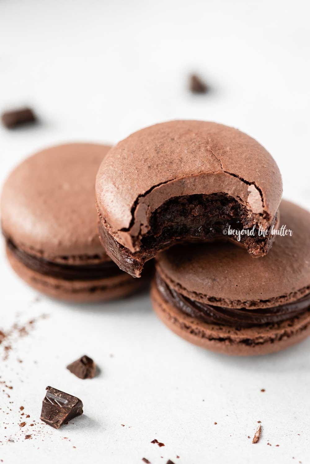 Angled image of stacked chocolate macarons with the top one having a bite taken out of it | All Images © Luyiz™
