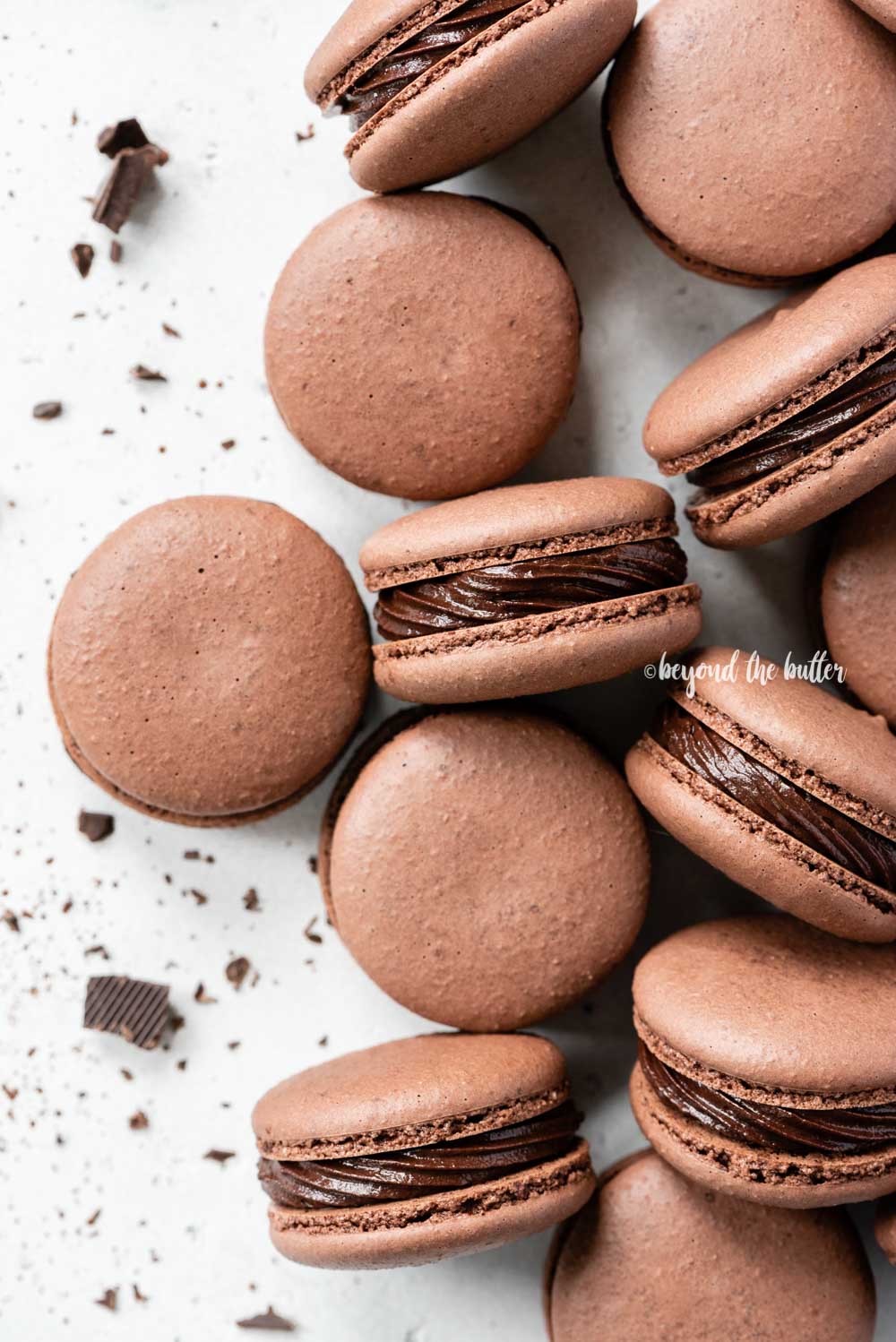 Overhead image of randomly placed dark chocolate macaons with bit of chocolate pieces around them | All Images © Luyiz™