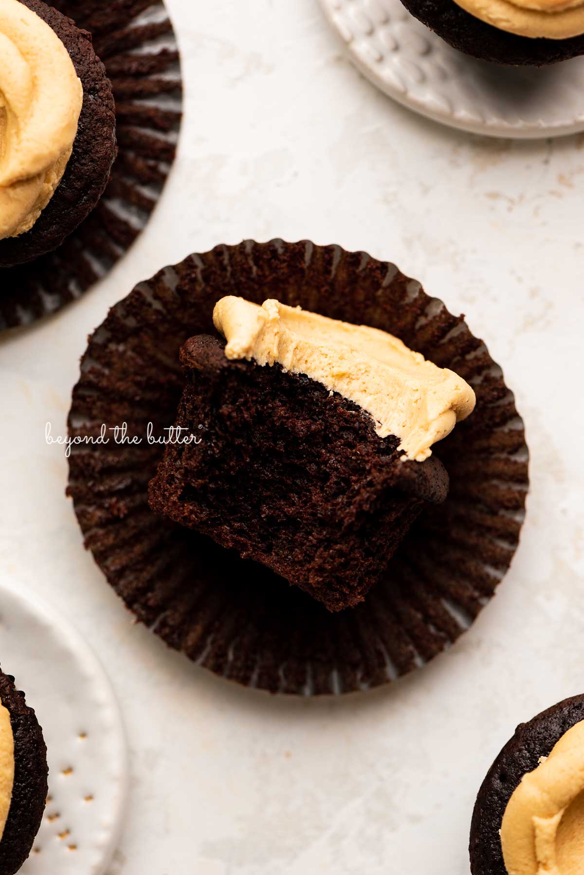 Unwrapped devil's food cupcake with peanut butter frosting with a bite taken out of it on white background | © Luyiz®