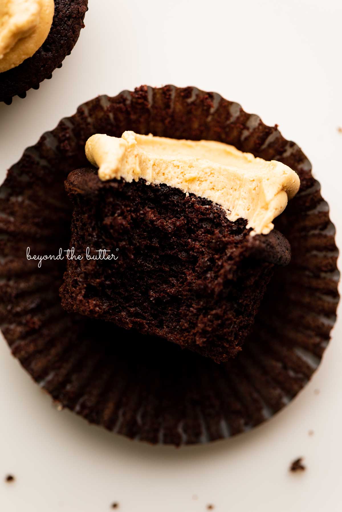 Unwrapped devil's food cupcake with peanut butter frosting with a bite taken out of it on white background | © Luyiz®