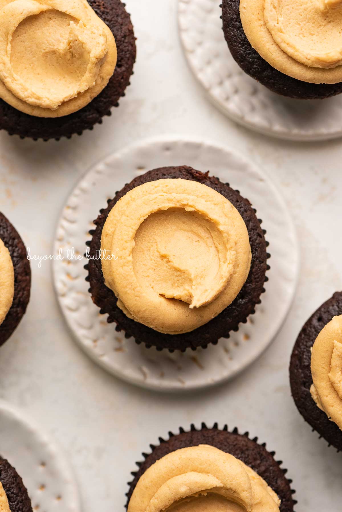 Devil's food cupcakes with peanut butter frosting with some on small dessert plates on white background | © Luyiz®