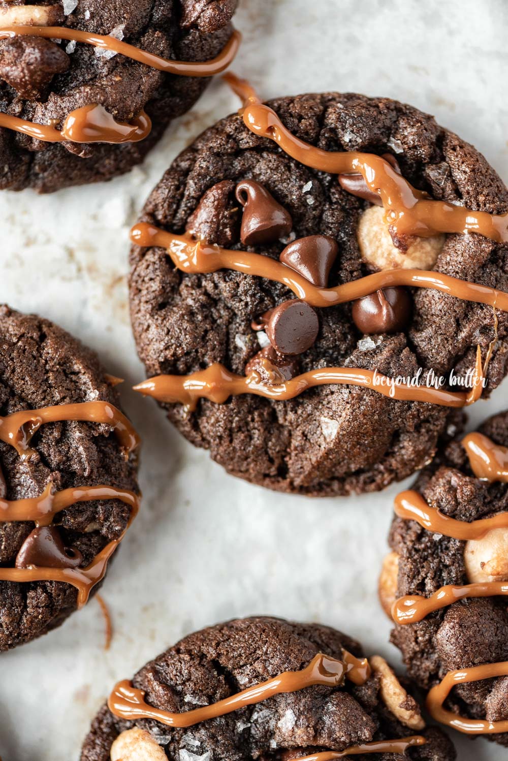Overhead image of just baked double chocolate salted caramel cookies on a baking sheet with caramel drizzled over the top of each cookie | All Images © Luyiz™