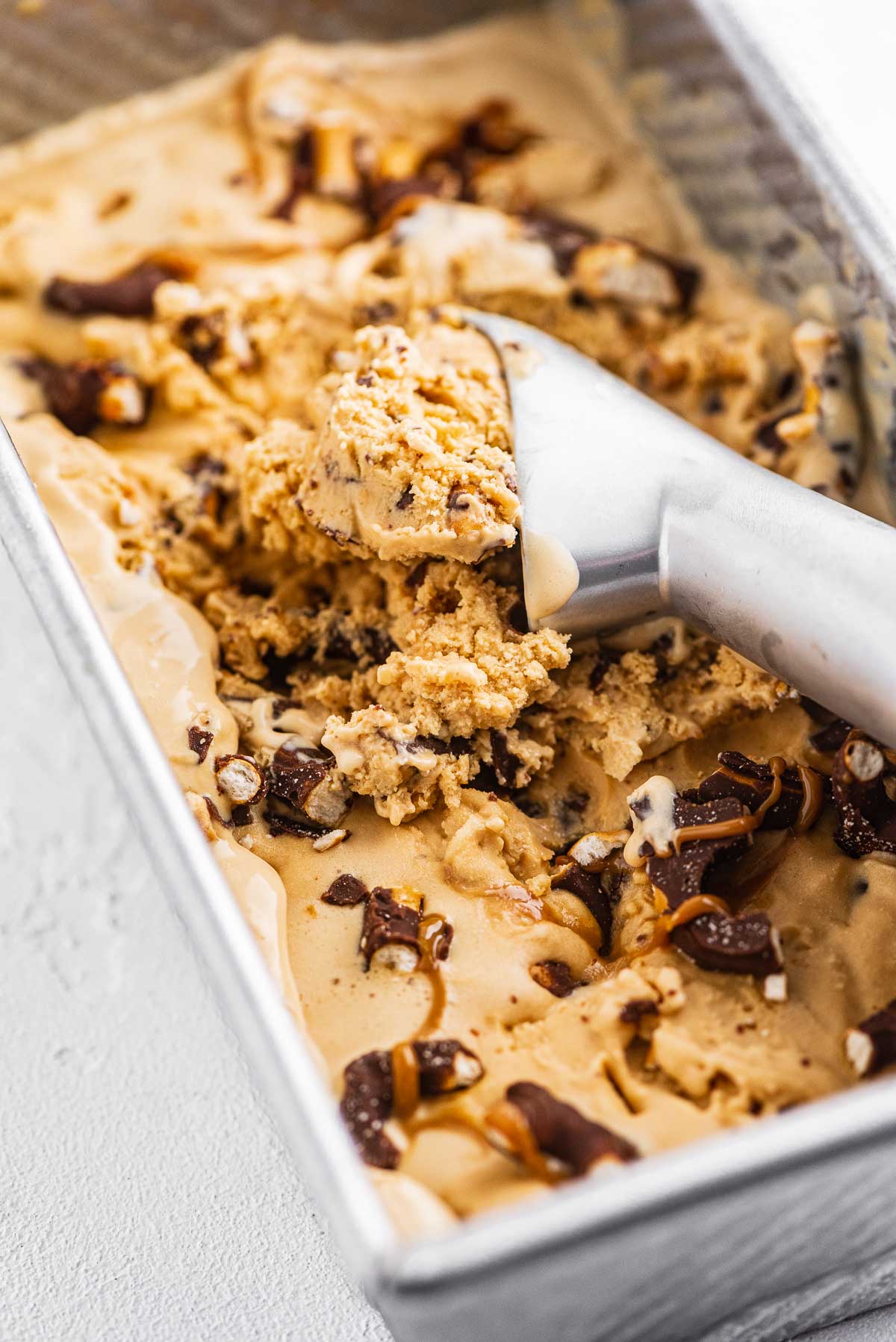 Ice cream sccop in a container of dulce de leche ice cream with chocolate covered pretzels | © Luyiz®