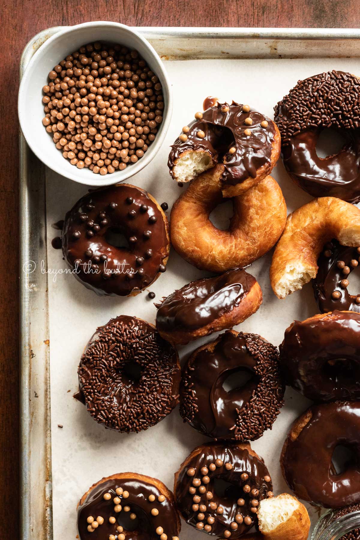 Parchment paper lined baking sheet with whole and half eaten donuts with salted caramel pearls in a bowl top left | All Images © Luyiz™
