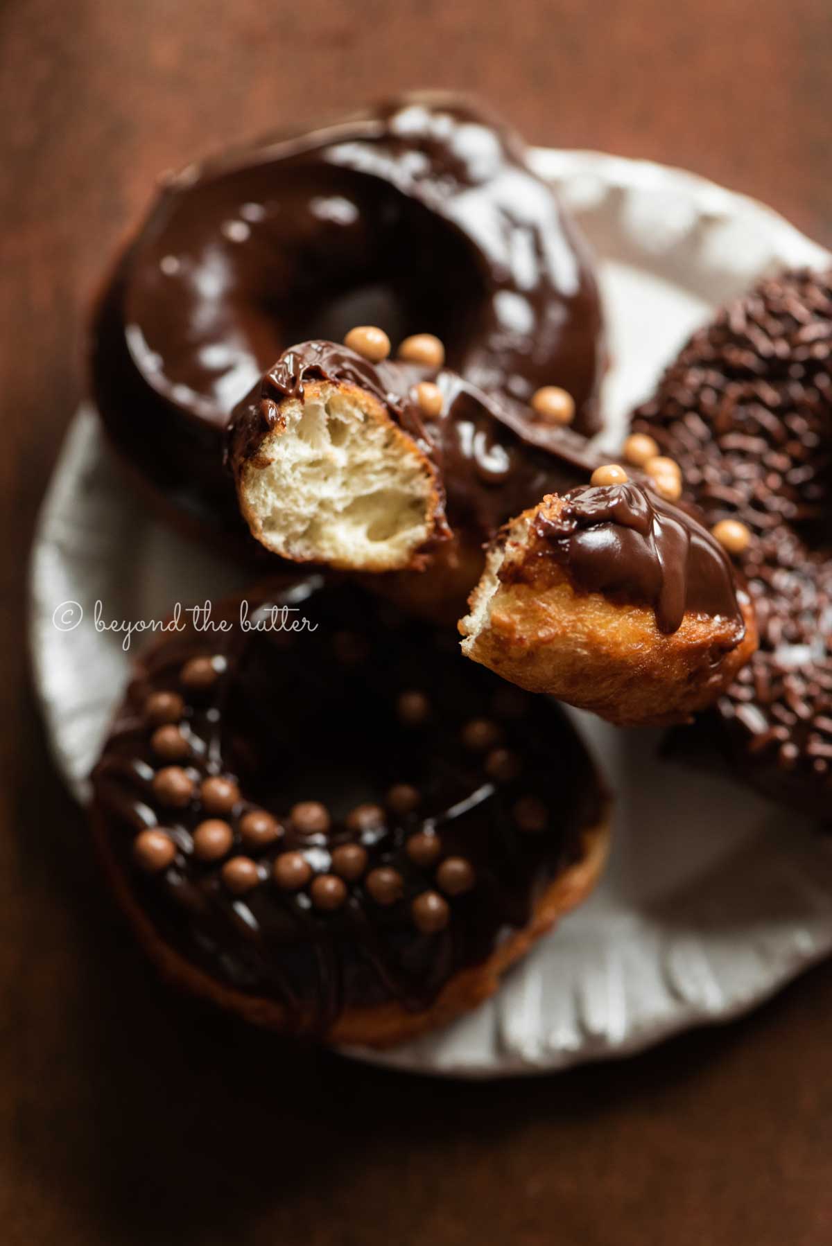 Chocolate glazed donuts stacked on a dessert plate with bite taken out of the top donut | All Images © Luyiz™