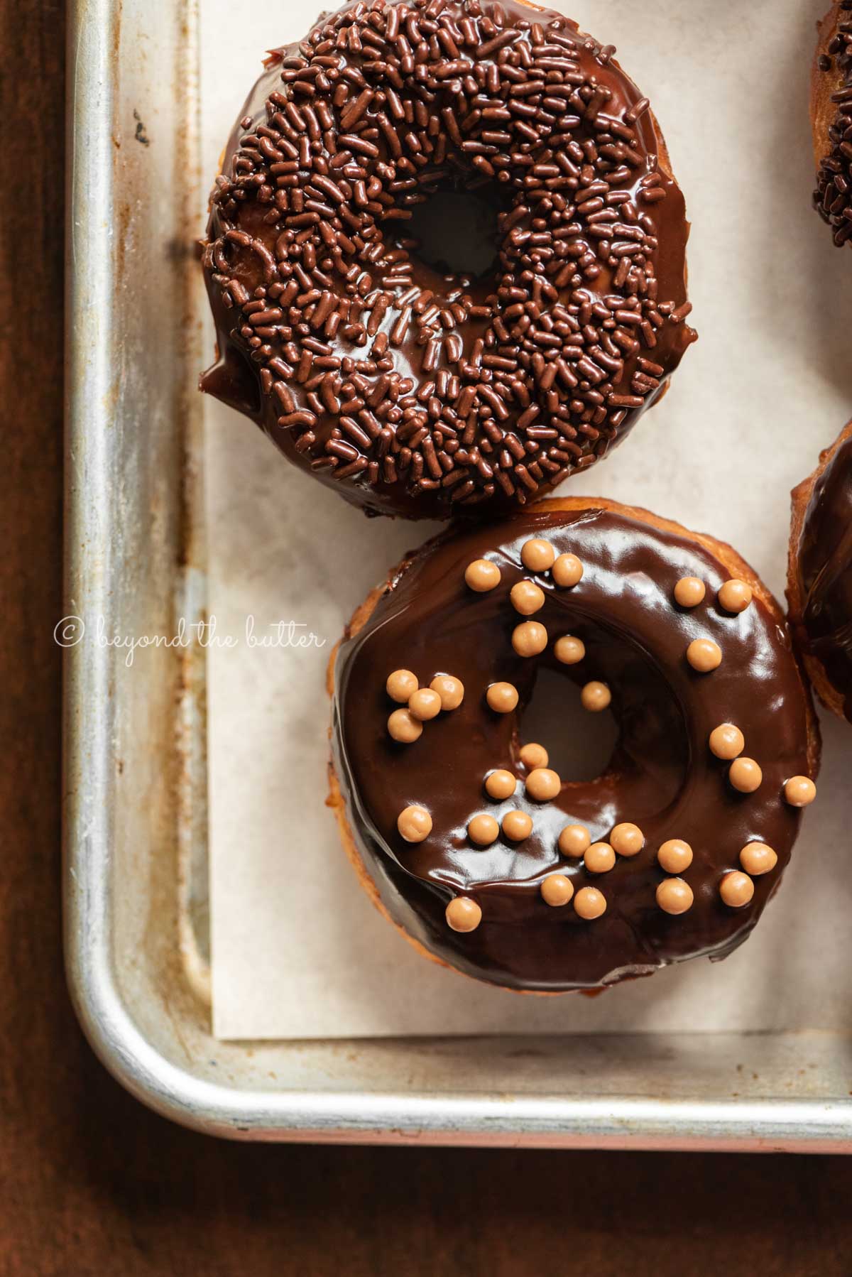 Chocolate glazed decorated donuts on a parchment paper lined baking sheet | All Images © Luyiz™
